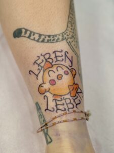 Farbenfrohes Cartoon-Tattoo mit dem Schriftzug „Leben Leben“ – gestochen von Tätowierer Jan